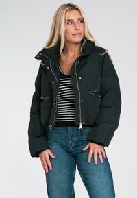 Czarna puchowa kurtka z wysokim kołnierzem, zapinana na zamek z przodu, z bocznymi kieszeniami. Noszona na paskowaną bluzkę, w zestawieniu z niebieskimi dżinsami. Gładka faktura.