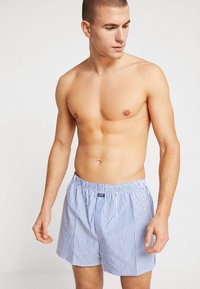 Blue and white striped swim shorts made of lightweight fabric, featuring an elastic waistband and a small logo tag at the front.