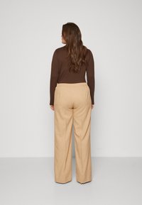 Brown long-sleeve top paired with beige wide-leg trousers featuring an elastic waistband, set against a neutral backdrop.