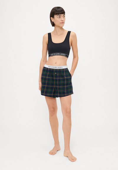 Sort sports-bh med en logo-bånd, parret med rutede shorts i marineblå, grøn og gul. Shortsene har en elastisk talje og knaplukning.