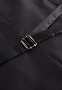 Tissu noir à la texture lisse orné d'une boucle métallique et d'une lanière, traversant en diagonale la surface dans un design élégant.