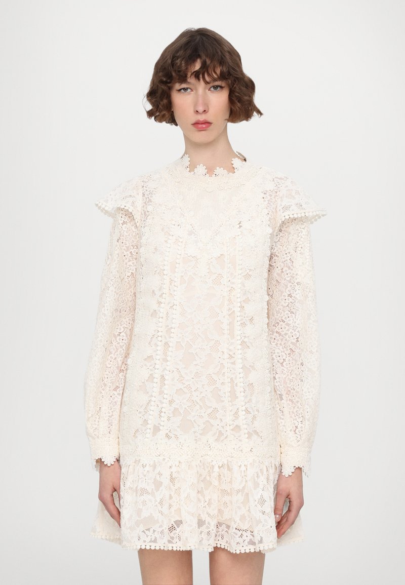 Spitzenkleid in Off-White mit langen Ärmeln, gerafften Schultern und einem ausgestellten Saum. Verfügt über florale Muster und gewellte Kanten.