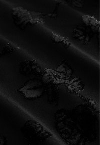 Fekete szövet, amely textúrált virágmintával rendelkezik, finom fényléssel. A minta leveleket és virágokat tartalmaz, ezáltal réteges hatást kelt.