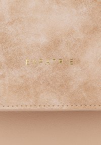 Portafoglio in faux pelle beige chiaro con finitura testurizzata, caratterizzato dal logo "EXPATRIÉ" in rilievo dorato centrato sulla parte anteriore.