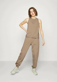 Top castanho sem mangas e calças de jogging a condizer. Tecido suave, corte descontraído, design minimalista. Sapatos de cor verde claro com uma superfície texturada.