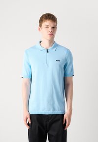 Camisa polo azul clara feita de tecido de malha macia, com colarinho com fecho éclair, mangas curtas e um pequeno logótipo preto "BOSS" no peito.