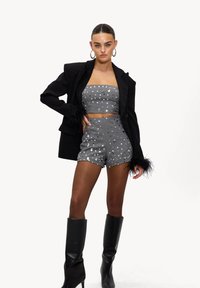 Ensemble crop top et shorts gris à sequins, associé à un blazer noir avec des poignets en fourrure et des bottes noires montantes.