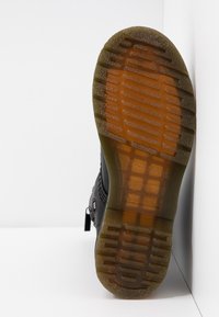 Semelle d'une botte noire en caoutchouc translucide marron présentant des motifs de grip rectangulaires et linéaires.
