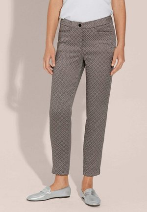 Woman wearing gray patterned slim-fit cropped trousers and metallic silver loafers, standing against a pale background.