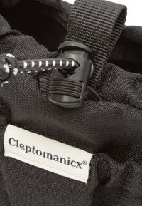 Schwarze Stofftasche mit strukturierter Oberfläche, verstellbarem Kordelzugverschluss und einem auffälligen Etikett mit dem Markennamen "Cleptomanicx."