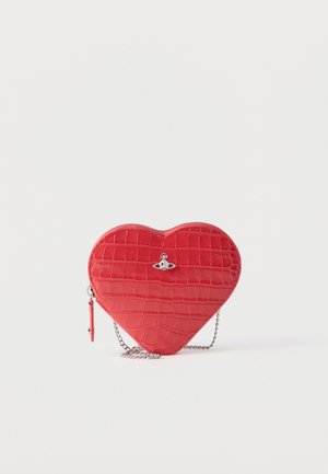 Sarkana sirds formas rokassoma ar krokodila ādas tekstūru, sudraba orb logo, rāvējslēdzēja aizdari un sudraba ķēdes siksnu uz baltas virsmas.