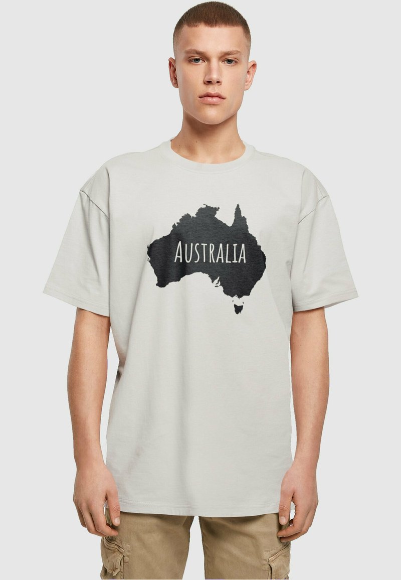 Ronde hals, T-shirt met korte mouwen in lichtbeige met een zwarte omtrek van Australië en het woord "AUSTRALIË" in vetgedrukte witte letters.