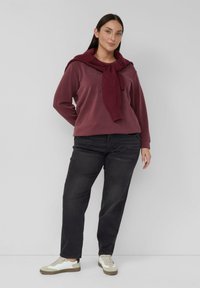 Bordowa bluza z okrągłym dekoltem i delikatną fakturą, w połączeniu z ciemnoszarymi dżinsami i białymi trampkami. Szalik zarzucony wokół szyi.