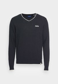 Czarny sweter z długim rękawem i dekoltem w kształcie litery V, z białym wykończeniem na kołnierzu, mankietach i dole, z małym białym haftowanym logo na piersi.