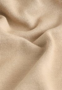 Tissu en maille beige avec une texture lisse, présentant un motif côtelé uniforme et une légère élasticité, mettant en valeur des fibres douces et naturelles.
