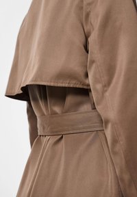 Barna ballonkabát, mely derékban övvel megkötős, puha tapintású, réteges kivitelű, hátul légies panellel. Tiszta, szabott vonalak jellemzik egészében.