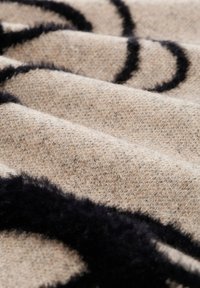 Kangasta bežillä, jossa on teksturoitu pinta, mustia, pörröisiä pyöreitä kuvioita, aseteltuna poimuille, mikä korostaa syvyyttä ja kontrastia.