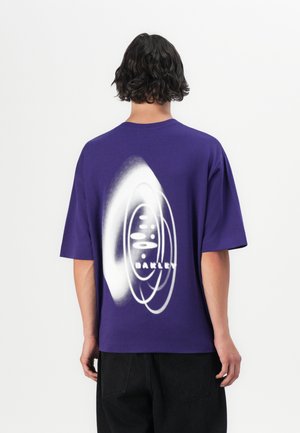 Purple short-sleeve t-shirt made of cotton, featuring a white graphic design and "OAKLEY" text on the back. Relaxed fit with a crew neck.