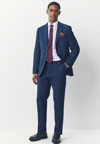 Dunkelblauer Anzug mit strukturierter Oberfläche, slim fit, einreihige Jacke, kombiniert mit einem weißen Hemd und einer burgunderfarbenen Krawatte. Abgerundet mit einem Einstecktuch.