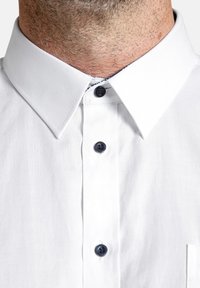 Weißes Hemd mit Knopfleiste, durchgehendem Design, spitzem Kragen und dunkelblauen Knöpfen. Mit einer Tasche auf der linken Brustseite.