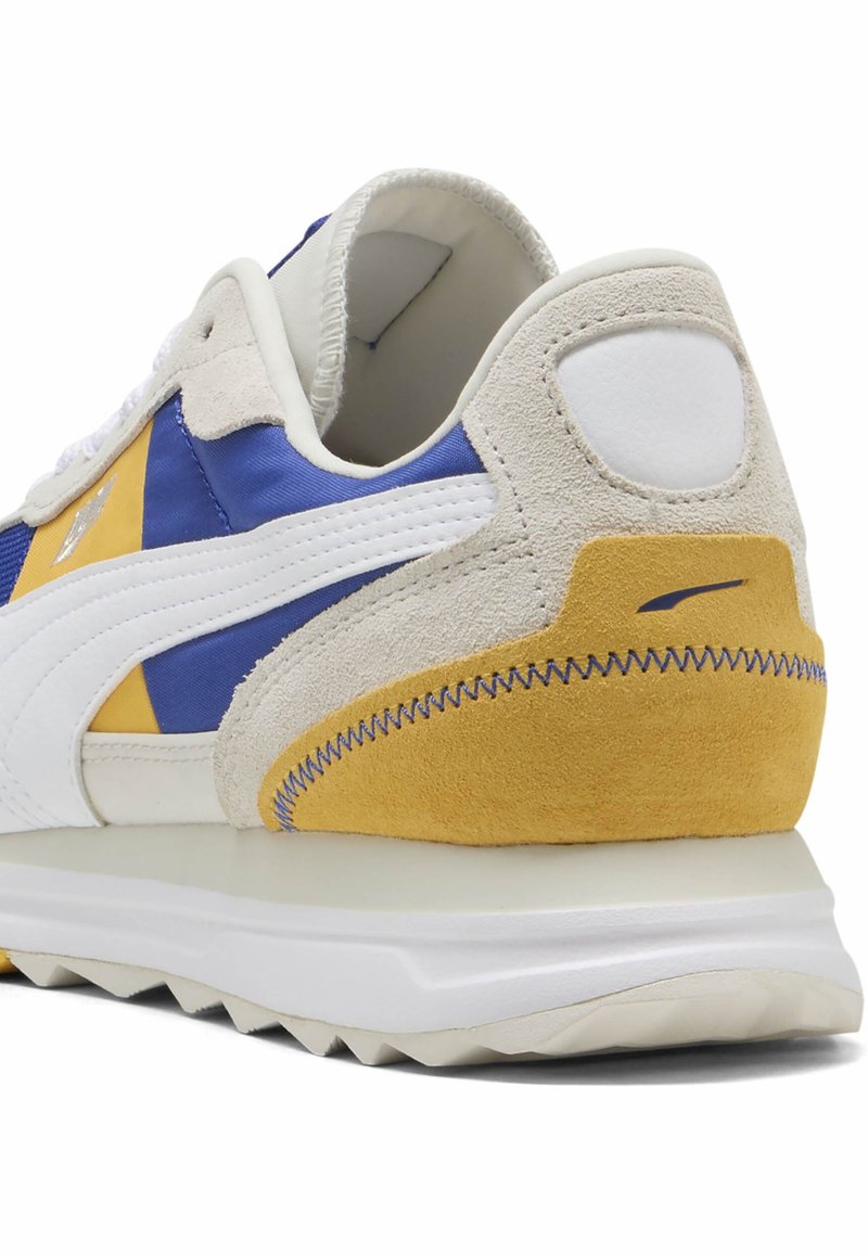 Sneaker z niebieskim satynowym wierzchem, białymi skórzanymi paskami i żółtymi zamszowymi akcentami. Posiada teksturowane pięty oraz kontrastowe szwy.