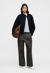 Μαύρο cropped σακάκι με στρογγυλή λαιμόκοψη και κουμπιά, ανοιχτό μπλε τοπ, γκρι παντελόνι με φαρδιά μπατζάκια και καφέ τσάντα, ολοκληρωμένα με άσπρα μυτερά παπούτσια.