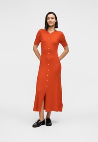 Ριμπ φόρεμα midi σε πορτοκαλί χρώμα με κοντά μανίκια, κουμπιά στο μπροστινό μέρος και σκίσιμο στο πλάι. Κατασκευασμένο από υφασμάτινη υφή, συνδυασμένο με μαύρα παπούτσια.