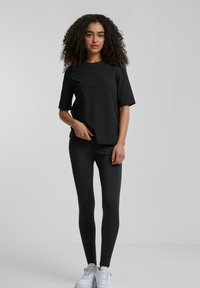 Svart bomulls t-skjorte med korte ermer, kombinert med svarte leggings. Outfiten har en avslappet passform og er supplert med hvite sneakers.