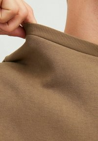 Tela de camiseta de algodón marrón con cuello acanalado, siendo tirada ligeramente; mostrando textura y forma sin detalles adicionales.