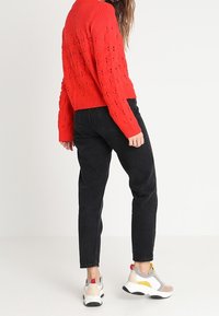 Červený pletený svetr s texturovaným vzorem, doplněný černými džíny s vysokým pasem a vícebarevnými sportovními teniskami.