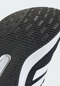 Black rubber shoe sole with textured tread pattern, white side accents, and a mesh fabric upper for breathability and support.