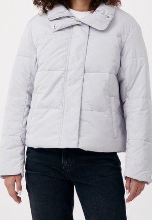 Kvinde iført en lysegrå quiltet dunjakke med sidelommer og lynlåslukning ved høj krave, kombineret med sorte bukser.