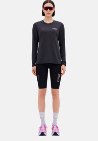 Schwarzes langärmeliges Sporthemd, schwarze Kompressionsshorts, graue Socken, pink- und grau-farbene Laufschuhe. CEP-Logo auf Hemd und Shorts.
