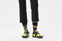 Chaussures jaunes et noires avec une semelle à pointes, associées à des chaussettes noires arborant un graphique coloré de "Star Wars", portées avec un pantalon noir.