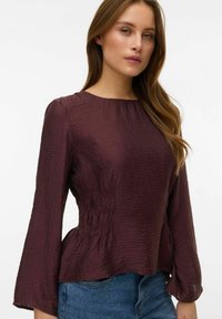 Mørkerød, tekstureret bluse med rund halsudskæring, lange ærmer og indsnævret talje, kombineret med en denim-nederdel.