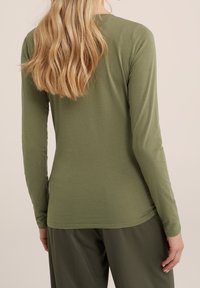 Long-sleeve shirt in olive green, made from soft, lightweight fabric. Fitted design with a round neckline and minimal stitching details.
