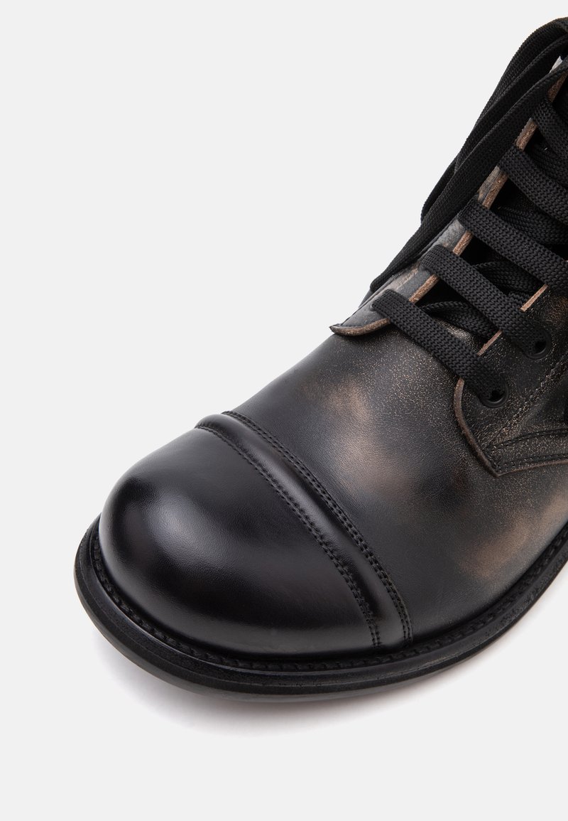 Close-up of the front part of a black leather lace-up boot with rounded toe and visible stitching on a white background.