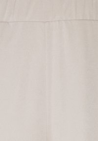 Lekko beżowa tkanina o gładkiej fakturze z delikatnym połyskiem. Materiał jest ułożony z lekkim marszczeniem u góry, bez widocznych elementów metalowych.