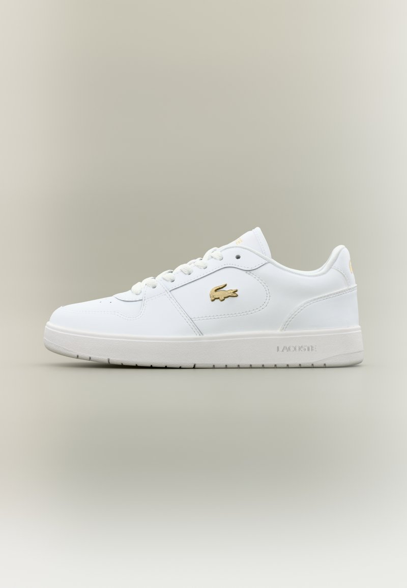Białe skórzane sneakersy z niską cholewką, okrągłym noskiem, sznurowanym zapięciem oraz złotym akcentem z logo Lacoste na boku.