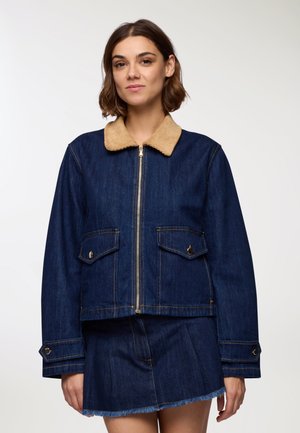 Giacca di jeans con colletto in corduroy color beige, chiusura con zip, due tasche frontali e dettagli di cucitura in bella vista. Design corto e informale.