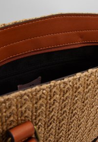 Gevlochten strohandtas met een gestructureerde beige buitenkant, bruine leren accenten, een gladde binnenvoering en een vak met rits.