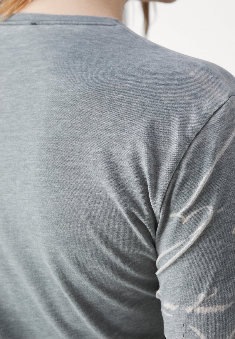 Plano detalle de la espalda de una persona con una camiseta gris suave que tiene patrones blancos sutiles en la manga y la zona del hombro.