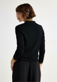 Sort sweater med en tætsiddende design, ribbede manchetter og en kontrasterende sennepsfarvet krave. Glat tekstur, ingen synlige mønstre eller hardware.