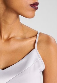 Ljusgrå satin camisole med tunna band och v-ringad design, som visar en slät textur och rena linjer vid halslinningen.