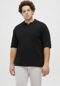 Juodas trumpomis rankovėmis polo marškinėliai su tekstūruotu raštu, su klasikiniu apykaklės dizainu ir laisvu siluetu, derinami su šviesiomis kelnėmis.