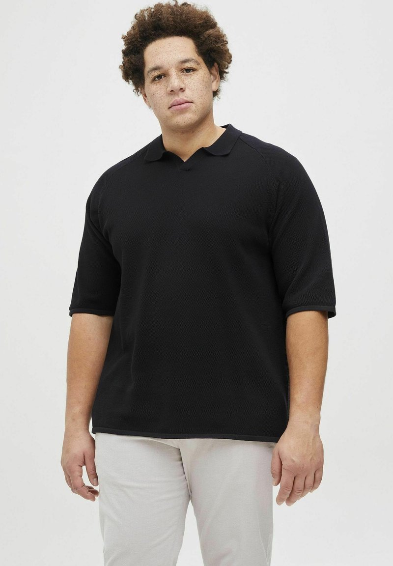 Juodas trumpomis rankovėmis polo marškinėliai su tekstūruotu raštu, su klasikiniu apykaklės dizainu ir laisvu siluetu, derinami su šviesiomis kelnėmis.