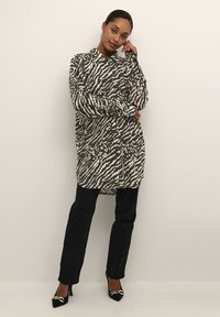 Langærmet skjorte i sort og beige zebrastribet mønster, parret med sorte jeans og højhælede sko med fletdetalje ved tåen.