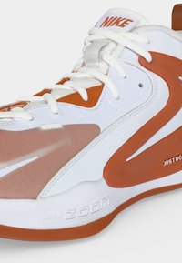 Κοντινό πλάνο σε λευκό και πορτοκαλί Nike Zoom sneaker με επίστρωση από δίχτυ, κορδόνια και κείμενο "Just Do It" στην πλευρά.