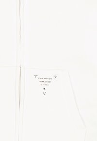 Weiße Kapuzenjacke mit Reißverschluss aus weichem Stoff, ausgestattet mit einem kleinen gedruckten Logo auf der Tasche und einem schlanken, schlichten Design.