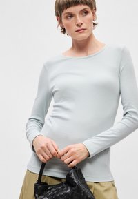 Top azul claro de manga longa com decote redondo e textura canelada. Combinado com uma mala tecida preta, com acabamento suave.